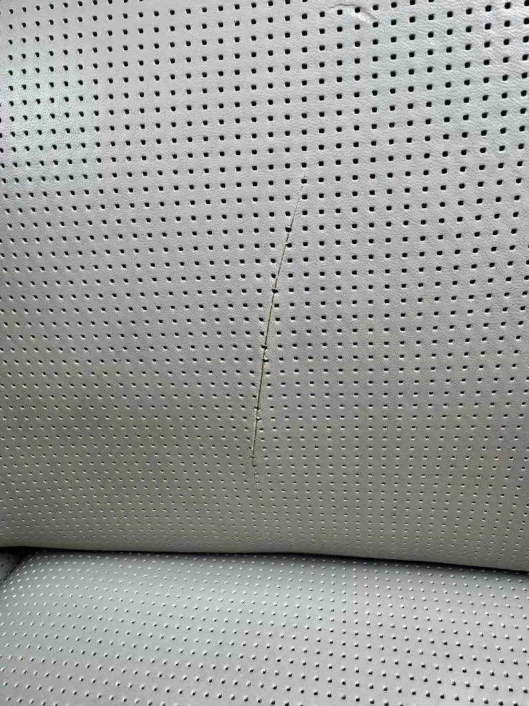 Pale tufted leather cushion with surface flaking and wear