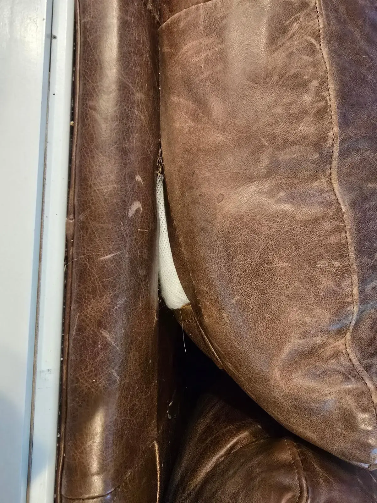 Pale tufted leather cushion with surface flaking and wear