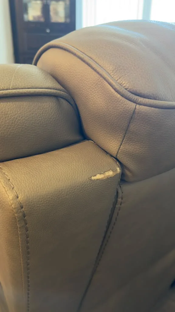 Pale tufted leather cushion with surface flaking and wear