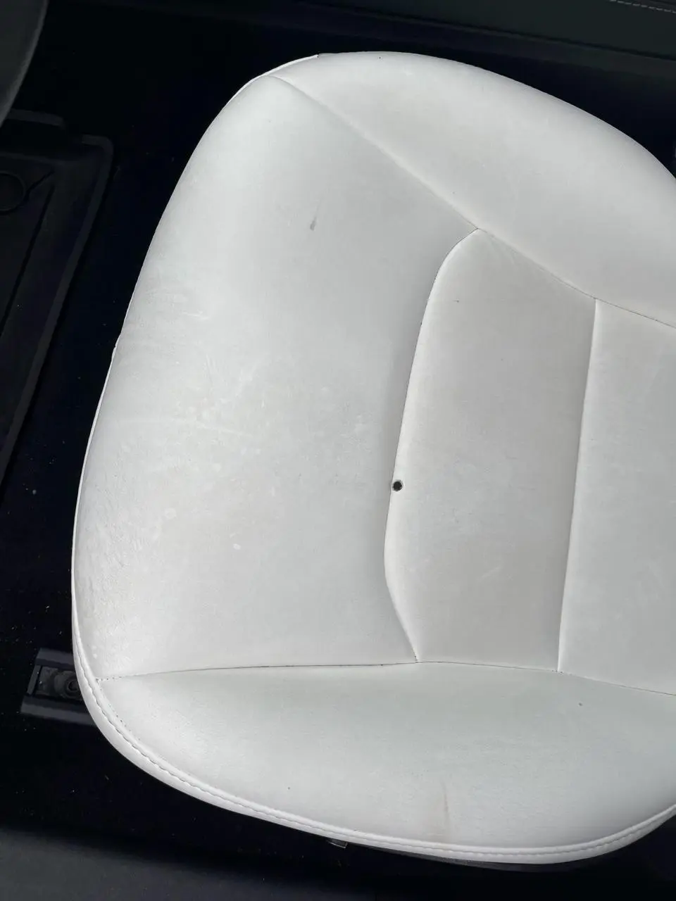 Dirty, stained white car seat with a puncture in the backrest